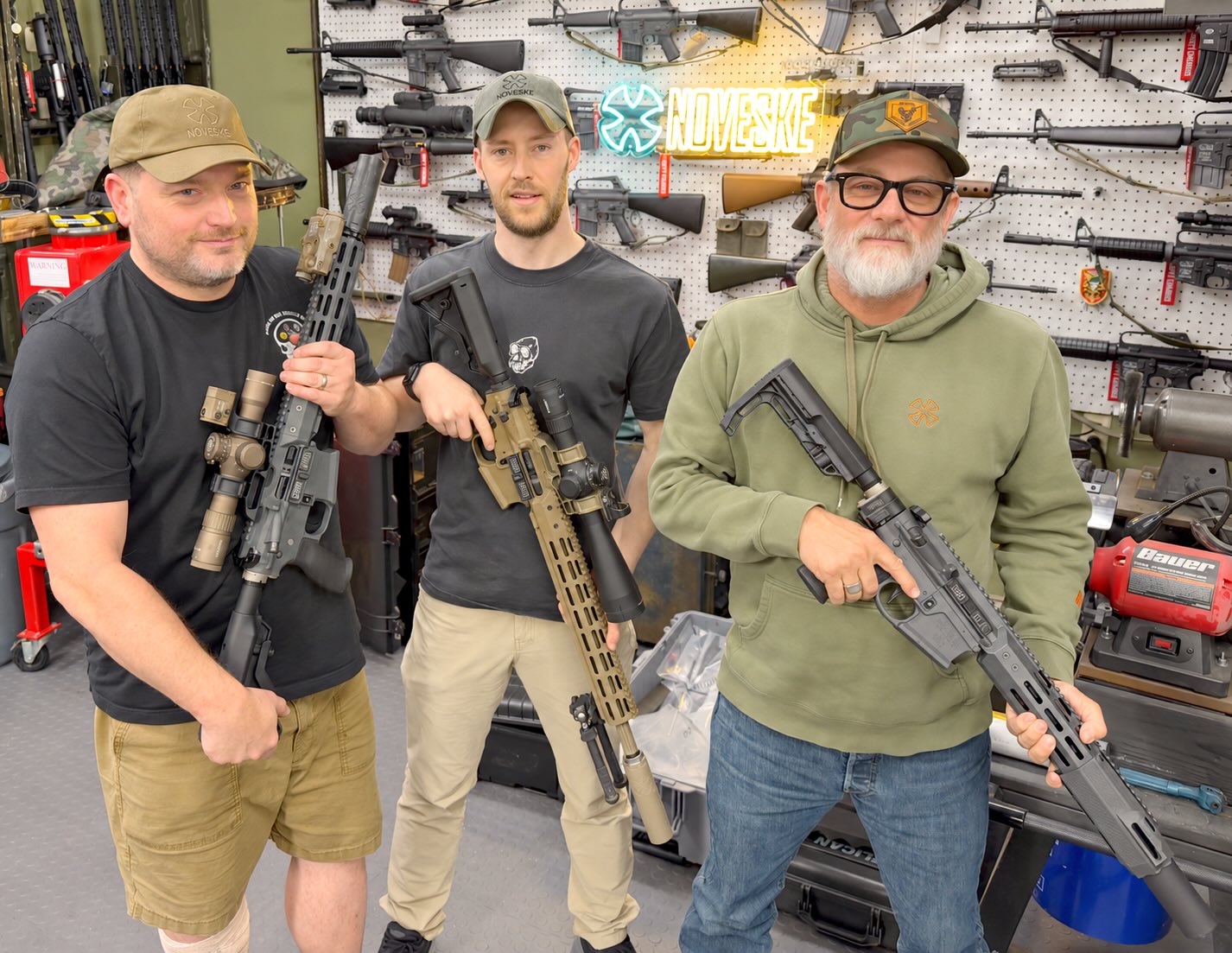 Chad of SOTAR, James of Quadradyn, and Jeff of Noveske standing side by side, each holding a rifle, beneath a Noveske sign